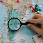 hand using magnifying glass over a map with pins
