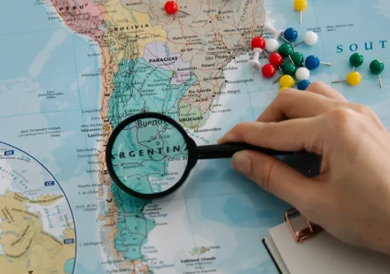 hand using magnifying glass over a map with pins