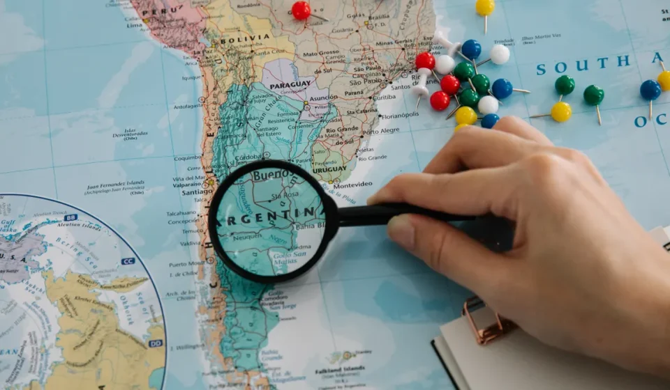 hand using magnifying glass over a map with pins