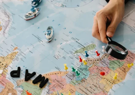 hand with magnifying glass over pinned world map