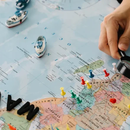 hand with magnifying glass over pinned world map