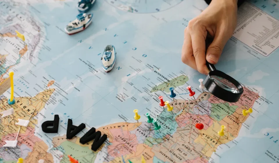 hand with magnifying glass over pinned world map